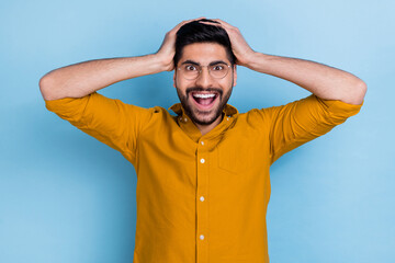 Photo of speechless staring crazy man wear yellow shirt hold hands on head unbelievable unexpected sale isolated on blue color background