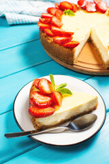 Piece of cheesecake with fresh strawberries jam and mint. Tasty homemade cheesecake on blue wooden background.