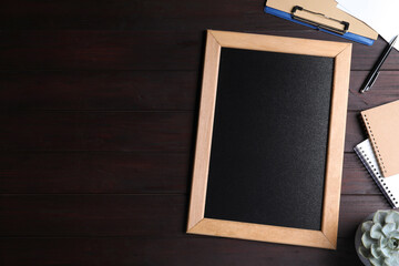 Clean small chalkboard, plant and stationery on wooden table, flat lay. Space for text