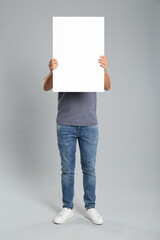 Man holding white blank poster on grey background. Mockup for design