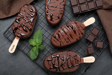 Delicious glazed ice cream bars, chocolate and mint on black table, flat lay