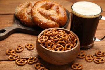 Tasty freshly baked pretzels, crackers and mug of beer on wooden table, closeup