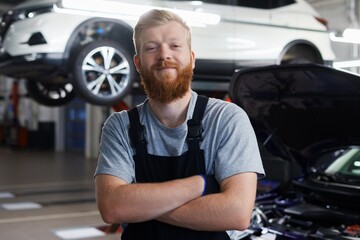 Portrait of a successful car mechanic in a clean uniform against the background of a car on a lift...