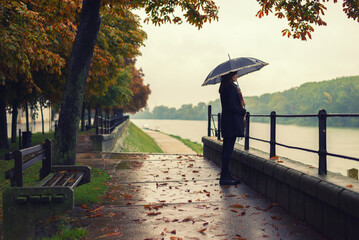 Young woman with umbrella walking in the autumn rain beside river