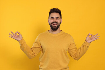 Young man meditating on yellow background. Zen concept