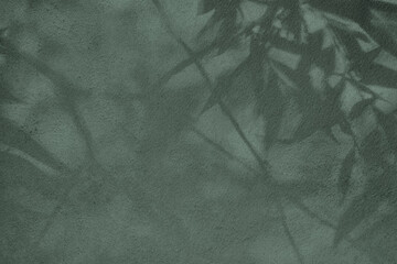 Abstract tree leaves shadows on gray green concrete wall texture with roughness and irregularities....