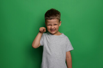 Angry little boy on green background. Aggressive behavior - obrazy, fototapety, plakaty