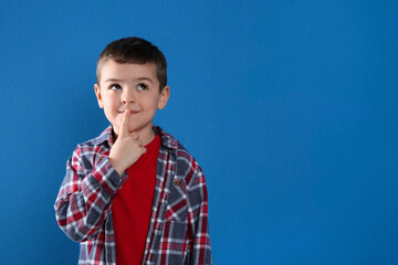 Thoughtful little boy on blue background, space for text