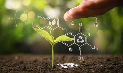 Illustration of chemical formulas and woman pouring water on young seedling in soil against blurred...