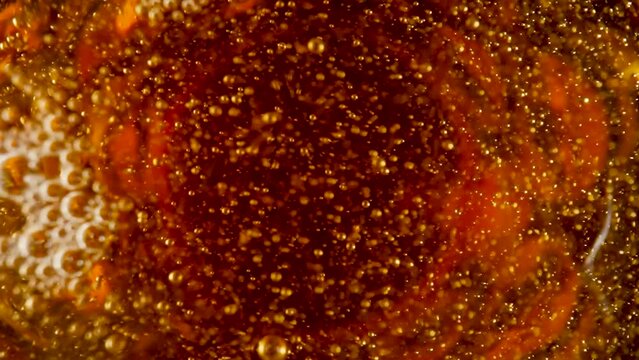 Top view of golden liquid with white foam and bursting bubbles. Macro shot of an amber foamy beer, cider or lagar. Carbonated soda or yellow oil. Beautiful textured beer background. Slow motion.