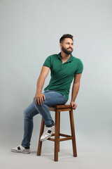 Handsome young man sitting on stool against light grey background