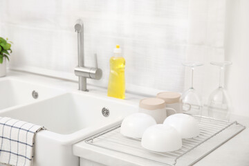 Drying rack with clean dishes near sink in stylish kitchen