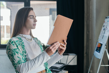 Queer designer holding paper folder in creative agency.