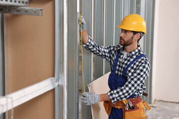 Professional builder in uniform working with measuring tape indoors