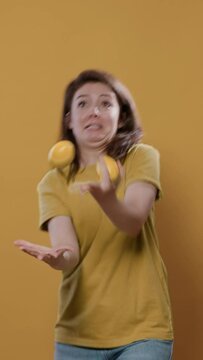 Playful woman acting silly trying to juggle oranges being funny while dropping them in studio. Individuality concept of person with fun and goofy personality showing juggle talent.