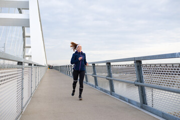 Young smiling woman running on the bridge footpath