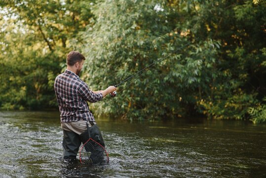 Man with fishing rod, fisherman men in river water outdoor. Catching trout fish in net. Summer fishing hobby