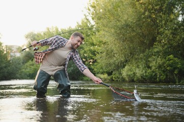 Fisherman catches a trout on the river in summer