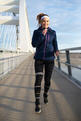 Young smiling woman running on the bridge footpath