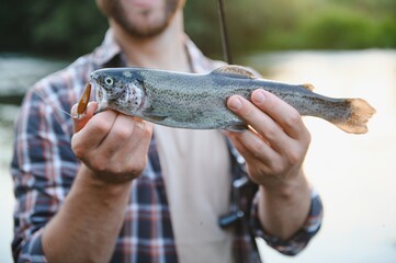 Happy fisherman holding a fish caught. Fishing on the beautiful river.