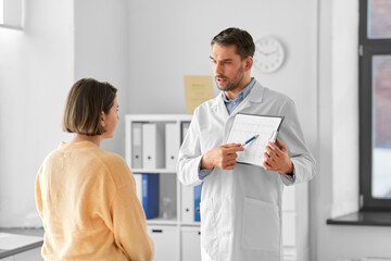 Obraz premium medicine, healthcare and people concept - male doctor or cardiologist with clipboard showing cardiogram to woman patient at hospital