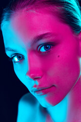 Closeup face of young beautiful girl with well-kept skin and without makeup isolated over dark background in neon light. Concept of beauty, art, cosmetics