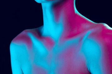 Close up female neck, collarbones and shoulders in pink neon light over dark background. Natural...