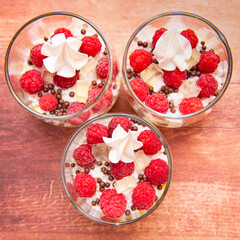Three verrines with pistachio cream, raspberries and white meringue on brown background. Image from above