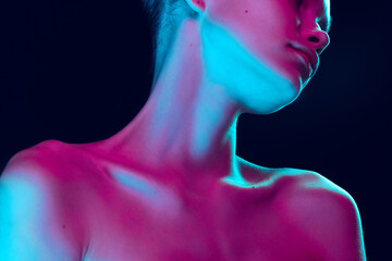 Close up female neck, collarbones and shoulders in pink neon light over dark background. Natural...