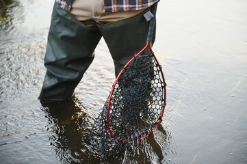 Fisherman hunting trouts in mountain river. Fishing net detail.