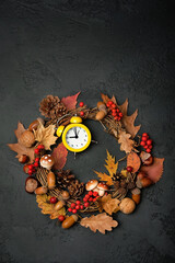 autumn decorative wreath with mushrooms, leaves, berries, acorns and alarm clock on dark background. symbol of autumn season. fall time. thanksgiving, mabon and halloween concept. Flat lay. copy space
