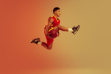 Portrait of young man, basketball player in motion, jumping, training isolated over orange studio...