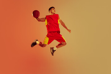 Portrait of muscular young man, basketball player in motion, throwing ball in a jump isolated over...