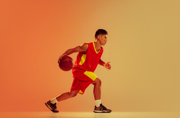 Portrait of young man, basketball player training isolated over orange studio background in neon...