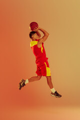 Fototapeta na wymiar Portrait of young man, professional basketball player training isolated over orange studio background in neon light. Jump shot