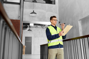 architecture, construction business and building concept - male supervisor in safety west with clipboard using voice command recorder on smartphone at office