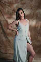 Brunette queer person in dress looking at camera on abstract background.