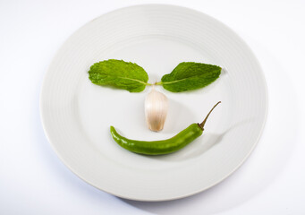 Funny face made with green herbs and spices on white plate. Fresh kitchen ingredients placed on a white plate.