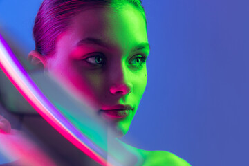 Portrait of young, beautiful and healthy girl with well-kept skin isolated on dark background in neon light. Art, fashion, style, facial expression