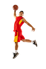 Portrait of young man, basketball player jumping, training, throwing ball into basket isolated over...