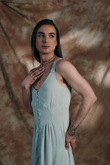 Young nonbinary person in dress posing on abstract background.