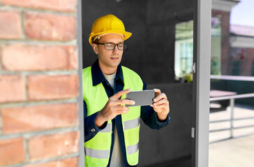 construction business and building concept - male builder in helmet and safety west with smartphone...