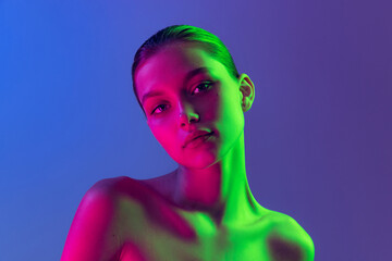Portrait of young, beautiful and healthy girl with well-kept skin isolated on dark background in neon light. Art, fashion, style, facial expression