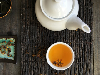 Bird eye view of a set up of an Asian tea ritual. White teapot and brewed herbal tea placed on a wooden mat.