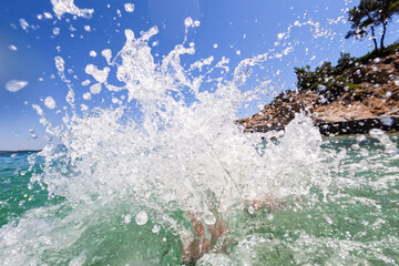 Happy child with swimming goggles splashing sea water at the camera. Fun on the summer holidays. 