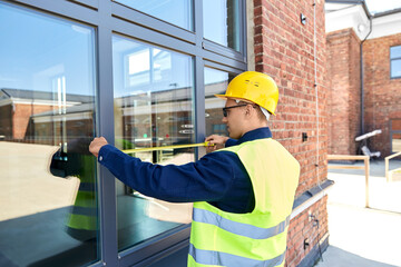 construction business and building concept - male builder with ruler measuring window