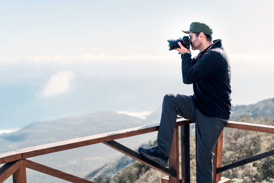 mature person with a camera sitting on lookout point taking pictures to the landscape over pacific ocean 