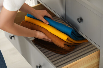 Woman putting clean clothes into drawer at home, closeup