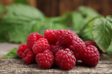 Fresh ripe raspberries and green leaves on wooden table, closeup