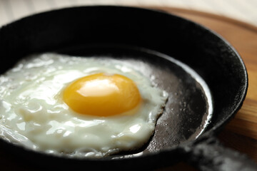 Frying pan with tasty cooked egg on wooden board, closeup